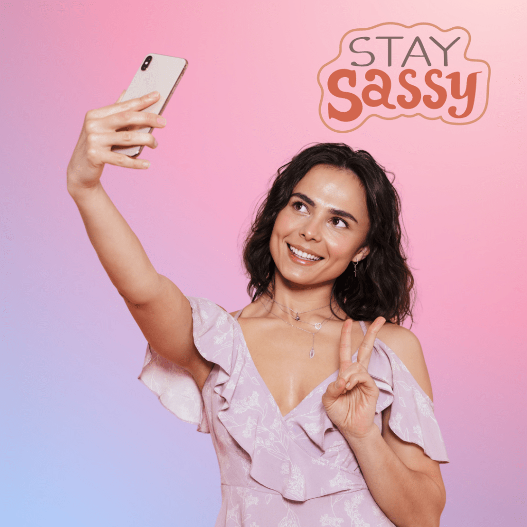 A woman in a light purple dress taking a selfie against a pink and purple gradient background, smiling and holding up a peace sign. The words "Stay Sassy" are written in a playful font above her, capturing a fun and confident mood perfect for a flirty caption.